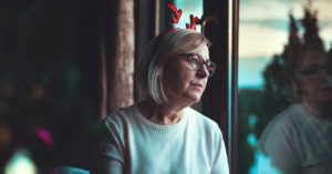 Senior woman who spent Christmas alone away from her family and friends due to the pandemic looks out the window sadly