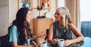 Older mother and daughter spending time together at home drinking coffee and discussing