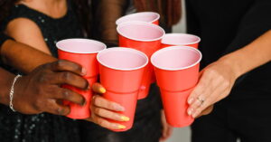 Waist up of six friends having fun and drinking alcohol during New Year party, isolated on white background. A group of cheerful friends of different nationalities clink glasses with red glasses at a party in the studio.