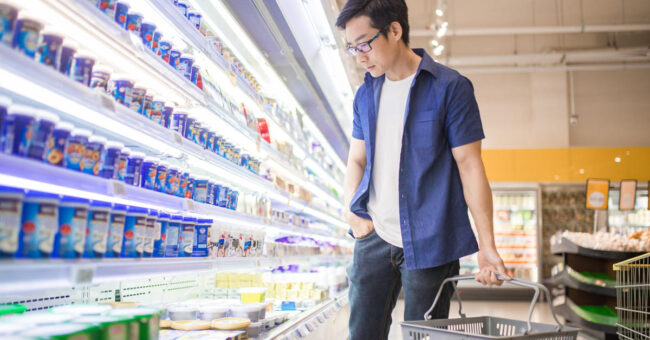 Blog Featured Image – Break Unhealthy Spending Habits A Chinese mature man holding basket and browses for products in the Frozen Goods Section.