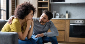 African American man comforting his girlfriend at home while she is looking upset - lifestyle concepts