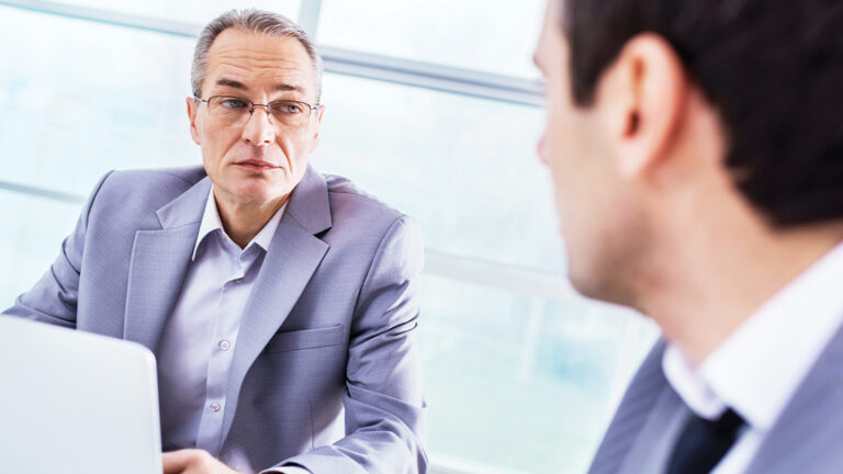 Blog Featured Image – Personal Hygiene Issues Two businessman in a meeting. Focus is on the mature man.