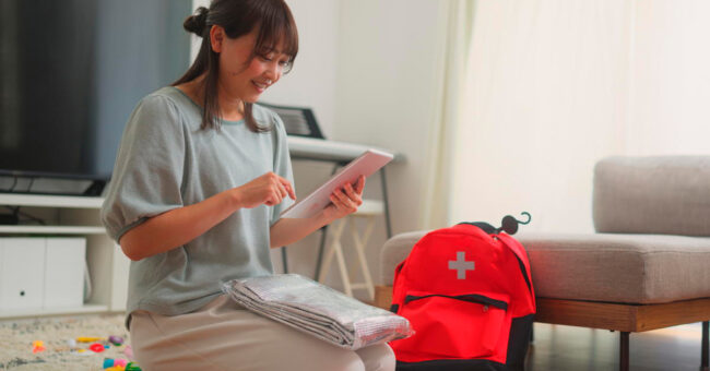 Blog Featured Image – Stay Prepared This Safety Month A woman is preparing an emergency bag in the living room at home.