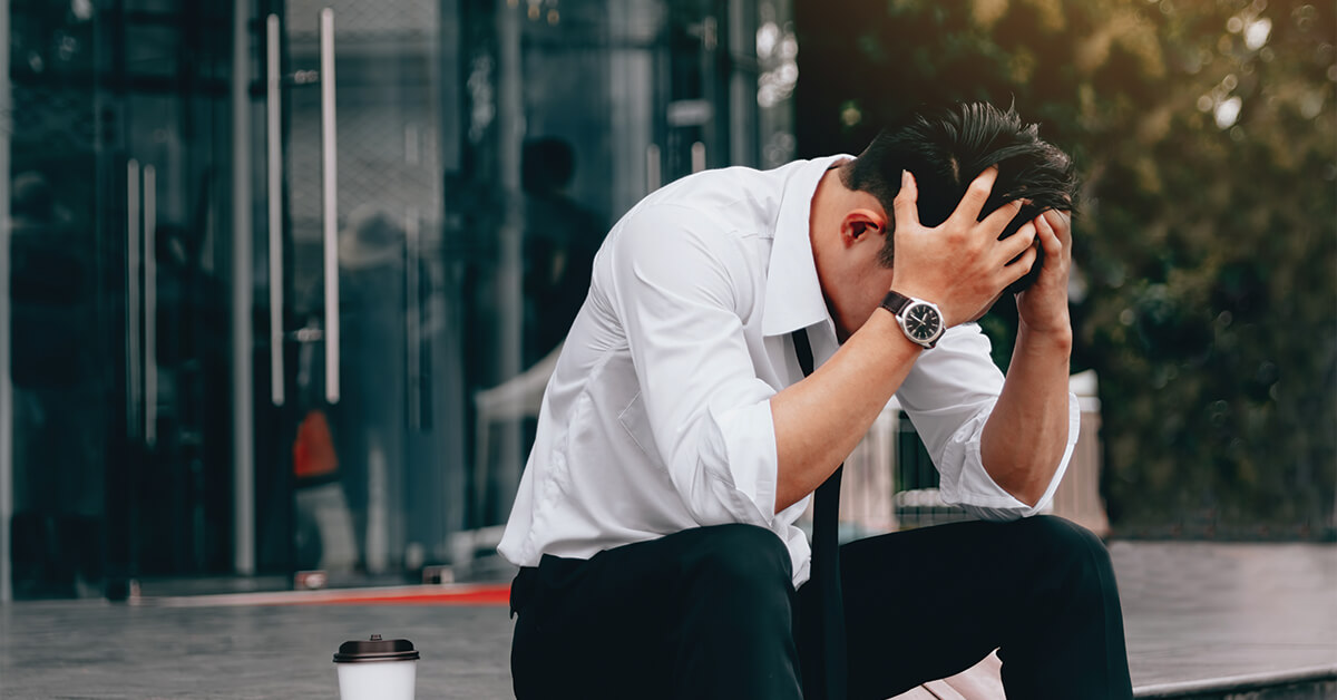 Asian young businessman stress sitting in front office with his hands covering his head against.