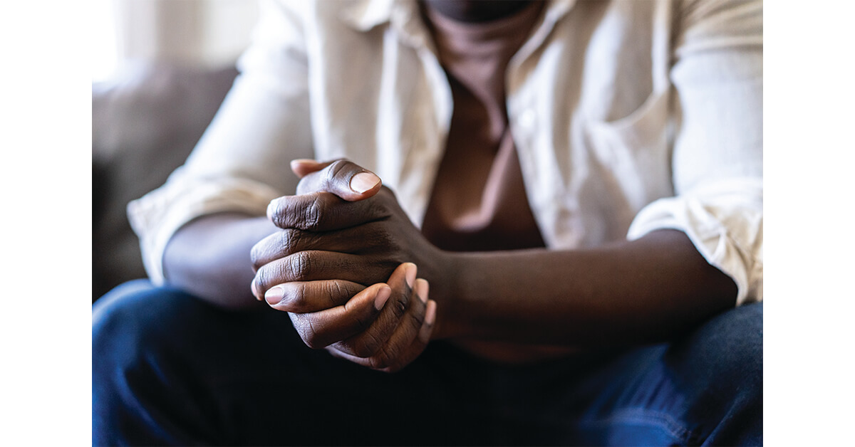 Close up of an unknown African-American man's claspling hands with the elbows leaning on his knees