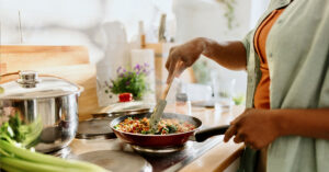 Woman cooking a colourful and nutritious quinoa stir-fry with mixed vegetables and a drizzle of olive oil.