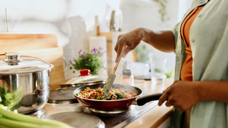 Blog Featured Image_Eat Cheaper with Meal Planning Woman cooking a colourful and nutritious quinoa stir-fry with mixed vegetables and a drizzle of olive oil.