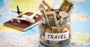 Travel budget concept. Travel money savings in a glass jar with compass, passport and aircraft toy on world map