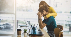 Coworker comforting stressed and discouraged woman in office.