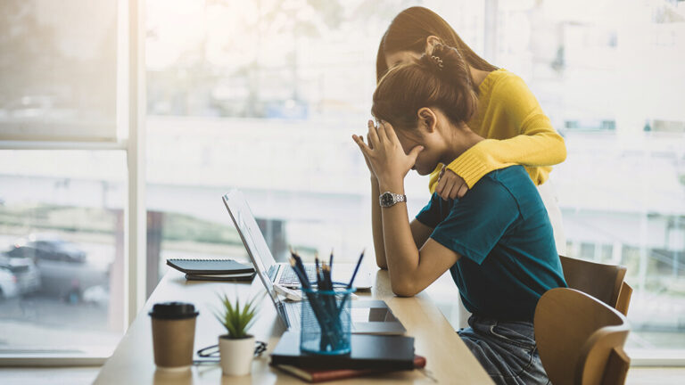Blog Featured Image_Supporting Your Team in a Time of Need Coworker comforting stressed and discouraged woman in office.