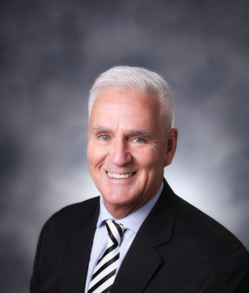 older white man in a suit with a smile and white hair 