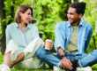 Young mixed-race couple friends boyfriend and girlfriend students spending time together on romantic date sitting on green lawn grass in city park walking outdoors. Love and relationship