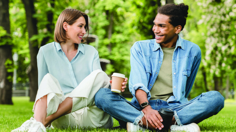 Dating on a Budget Young mixed-race couple friends boyfriend and girlfriend students spending time together on romantic date sitting on green lawn grass in city park walking outdoors. Love and relationship
