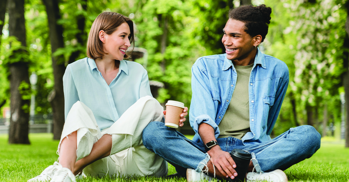 Young mixed-race couple friends boyfriend and girlfriend students spending time together on romantic date sitting on green lawn grass in city park walking outdoors. Love and relationship