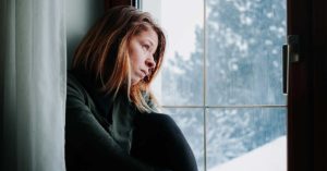 Sad woman sitting by the window looking outside