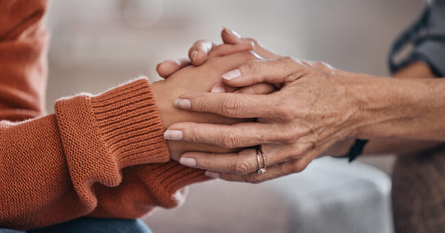 Episode 16 – Mental Health Around the World, Part 1 Women, holding hands and closeup for therapy, mental health support or consultation for problem on sofa. Woman, helping hand and psychologist for wellness conversation, advice or care for depression