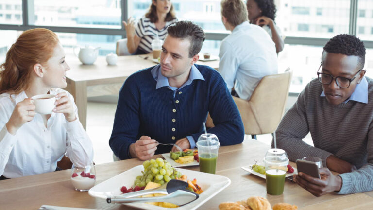 Featured Image – Respectful Workplace Behavior During an Election colleagues from mixed race backgrounds indulging in lunch in a contemporary office space. Seated at a table, engaging in conversation about the election and appreciating shared moments.