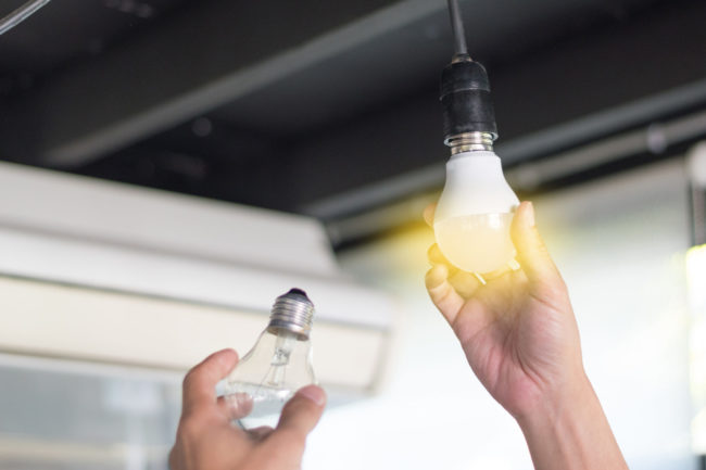 Power saving concept. Asia man changing compact-fluorescent (CFL) bulbs with new LED light bulb. changing lightbulb