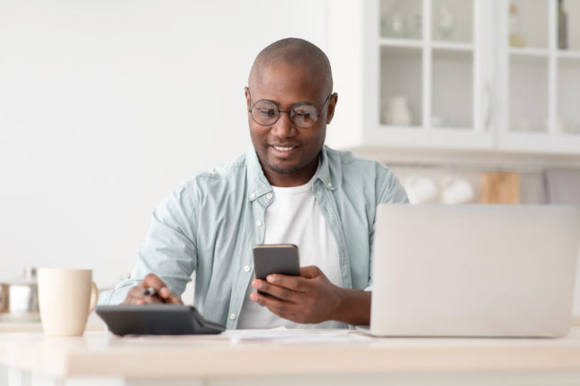 Savings and finances concept. Mature black man using calculator, phone and laptop computer man using phone, laptop, and calculator