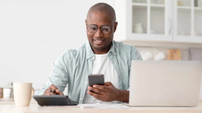 Savings and finances concept. Mature black man using calculator, phone and laptop computer man using phone, laptop, and calculator