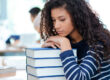 College student that's scared of school resting her head on textbooks