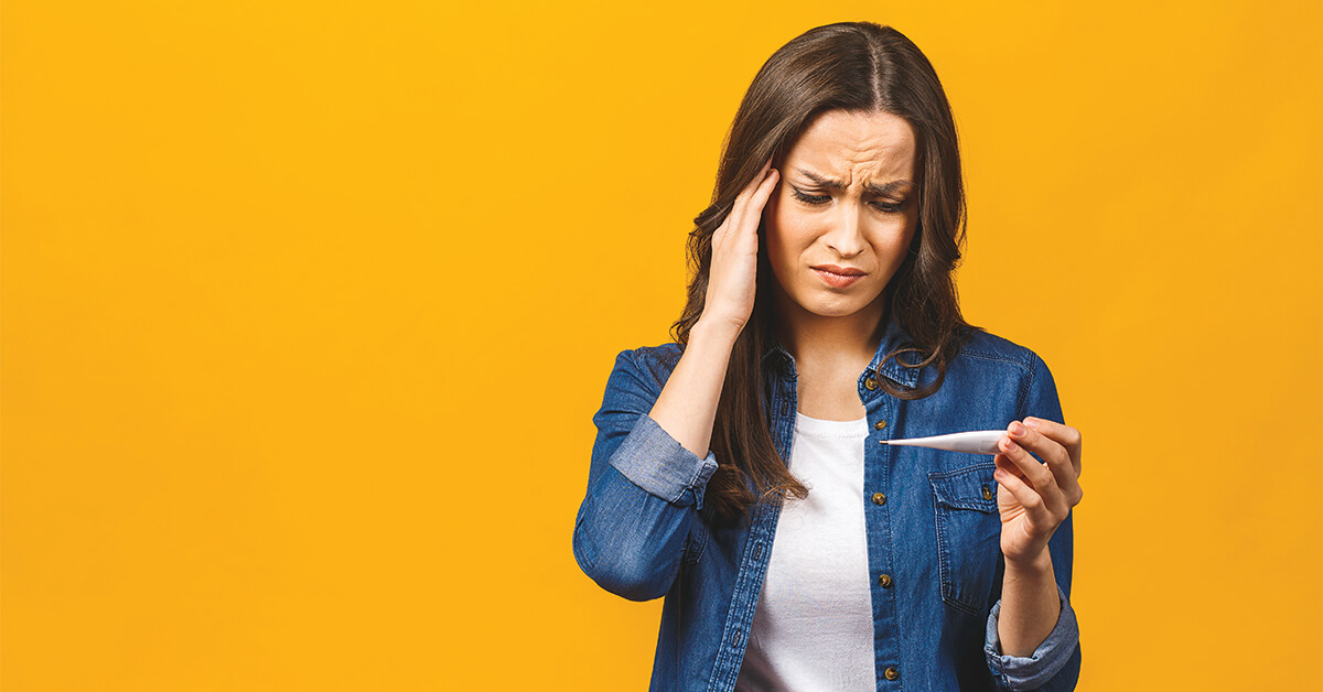 Young woman having flue taking thermometer. Isolated against yellow background. Beautiful young woman is sick with a high temperature, a thermometer, isolated close-up. Cold, flu concept.