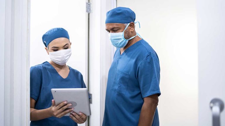 Healthcare coworkers walking and analyzing digital tablet at hospital – wearing face mask Healthcare coworkers walking and analyzing digital tablet at hospital - wearing face mask