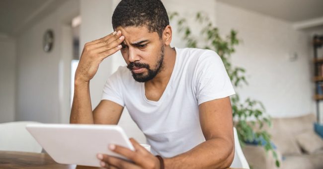 Soft-Skills-For-Management-Success Worried mixed ethnicity man sitting in a living room, contemplating with a digital tablet.