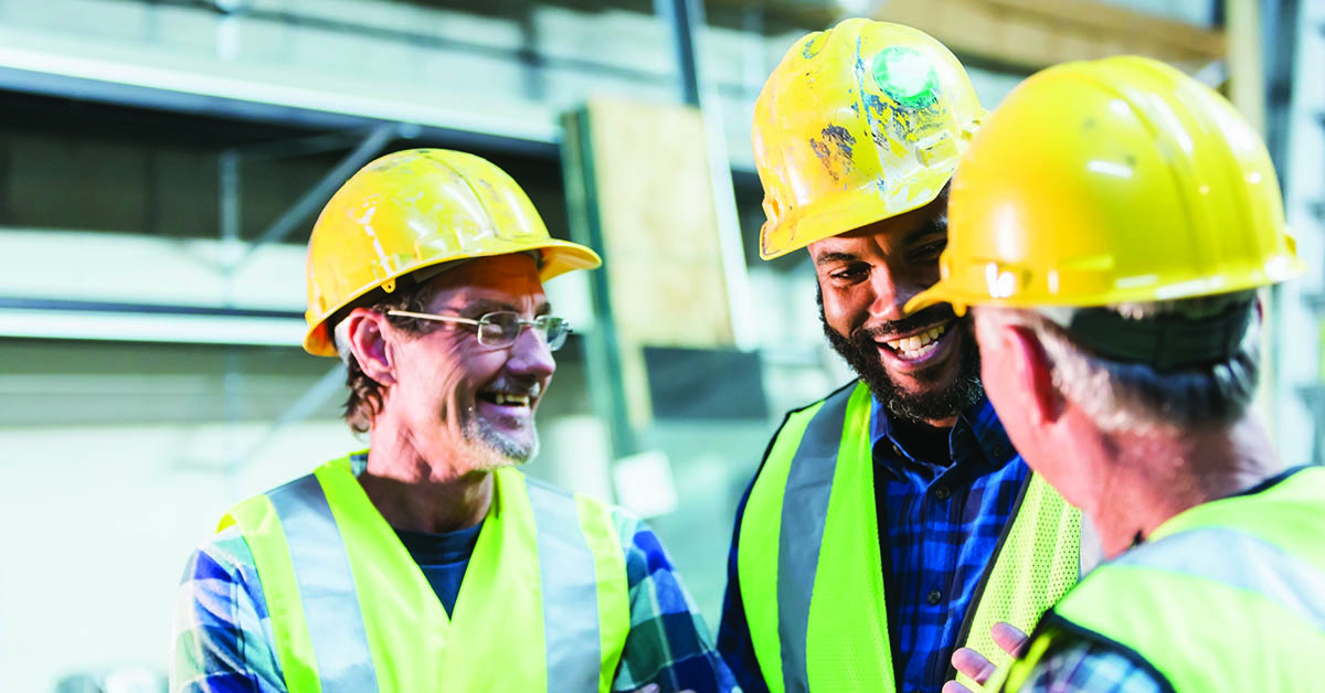 A group of three multi-ethnic men wearing hard hats and safety vests having a meeting. The main focus is on the African American man who is in his 30s.