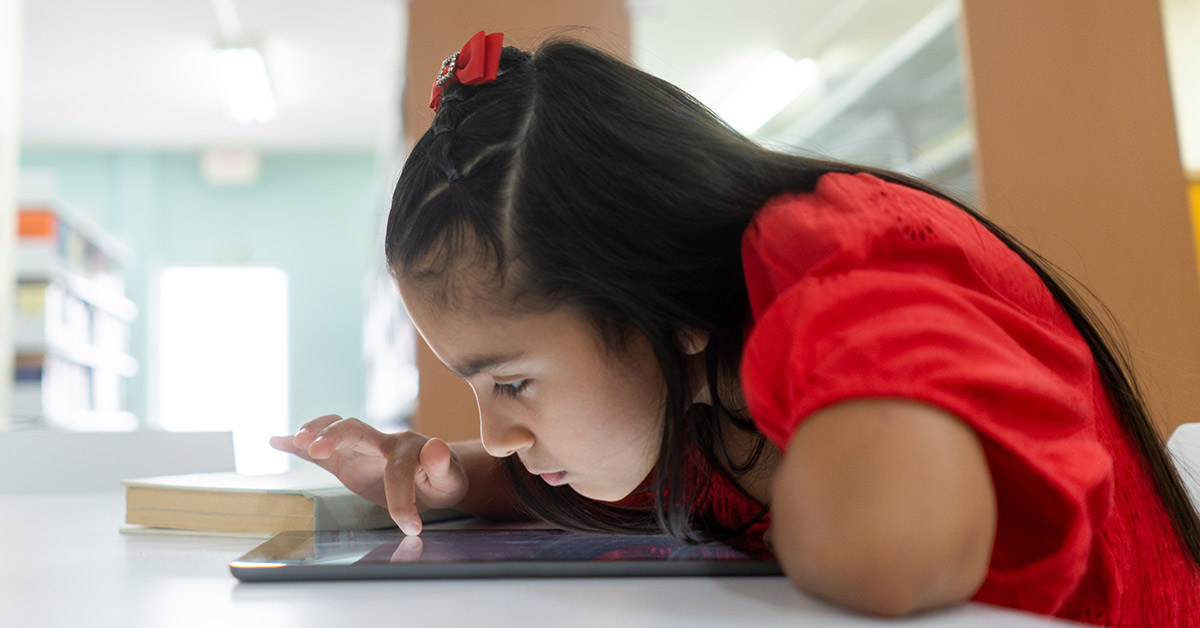 A shortsighted little latin girl using a digital tablet with her face close to the screen. A shortsighted little latin girl using a digital tablet with her face close to the screen.