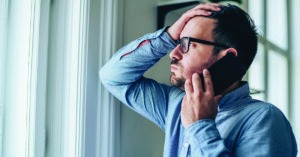 Worried businessman with hand on forehead talking on mobile phone in his office.