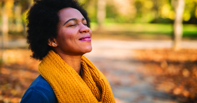 be-optimistic-featured-image Happy mid adult African American woman enjoying a walk on autumn day in the park. Close up of tranquil woman inhaling and relaxing at the park.