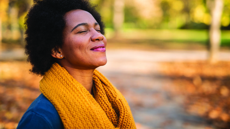 be-optimistic-featured-image Happy mid adult African American woman enjoying a walk on autumn day in the park. Close up of tranquil woman inhaling and relaxing at the park.