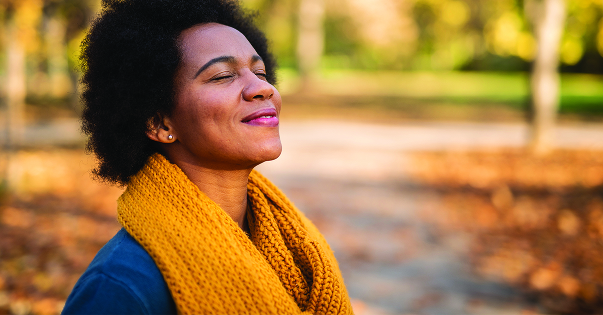 be-optimistic-featured-image Happy mid adult African American woman enjoying a walk on autumn day in the park. Close up of tranquil woman inhaling and relaxing at the park.