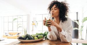 Young african american woman drinking green juice with reusable bamboo straw in loft apartment