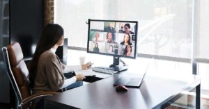 A group of creative professionals meet virtually to discuss and brainstorm ideas. A young female creative professional is working in an office while talking with colleagues who are telecommuting from their homes.