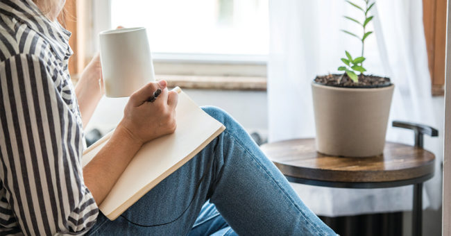 daily-questions-featured-image A young woman takes a break to do something analog like writing in her journal and drinking tea. This is a healthy practice for those who experience anxiety.