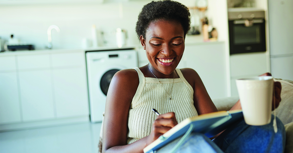 gratitude-journaling Shot of a young woman having tea and writing in a notebook on the sofa at home