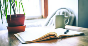 An open journal and pen on a table with a cup of tea for a mental health break