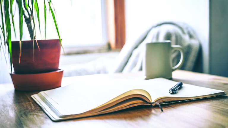 managing-negative-self-talk-featured-image An open journal and pen on a table with a cup of tea for a mental health break