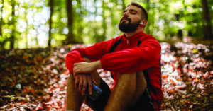 Portrait of relaxed young man with bluetooth headphones in forest