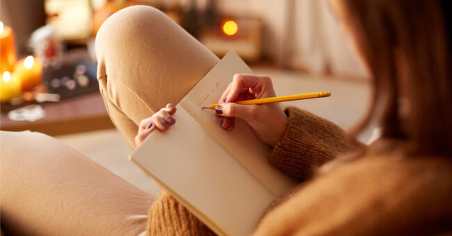 close up of young woman with pencil writing to diary and resting her feet on table at cozy home close up of young woman with pencil writing to diary and resting her feet on table at cozy home