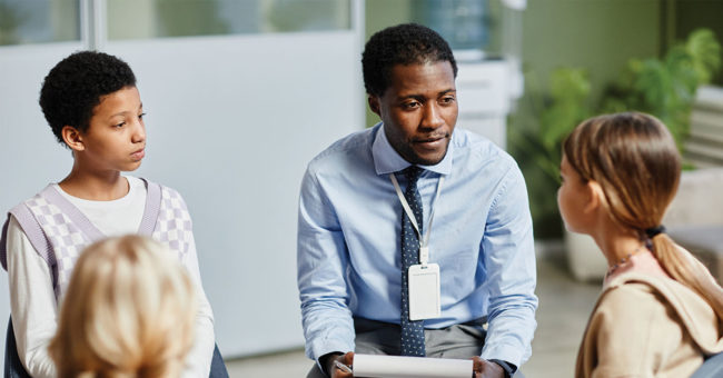 Portrait of young African-American psychologist listening to children in support group circle Portrait of young African-American psychologist listening to children in support group circle