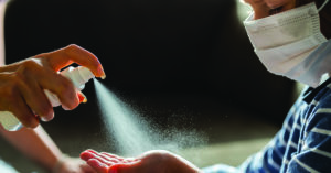 Unrecognizable single parent spraying hand sanitizer to her little boy's hand. Boy is with face mask.